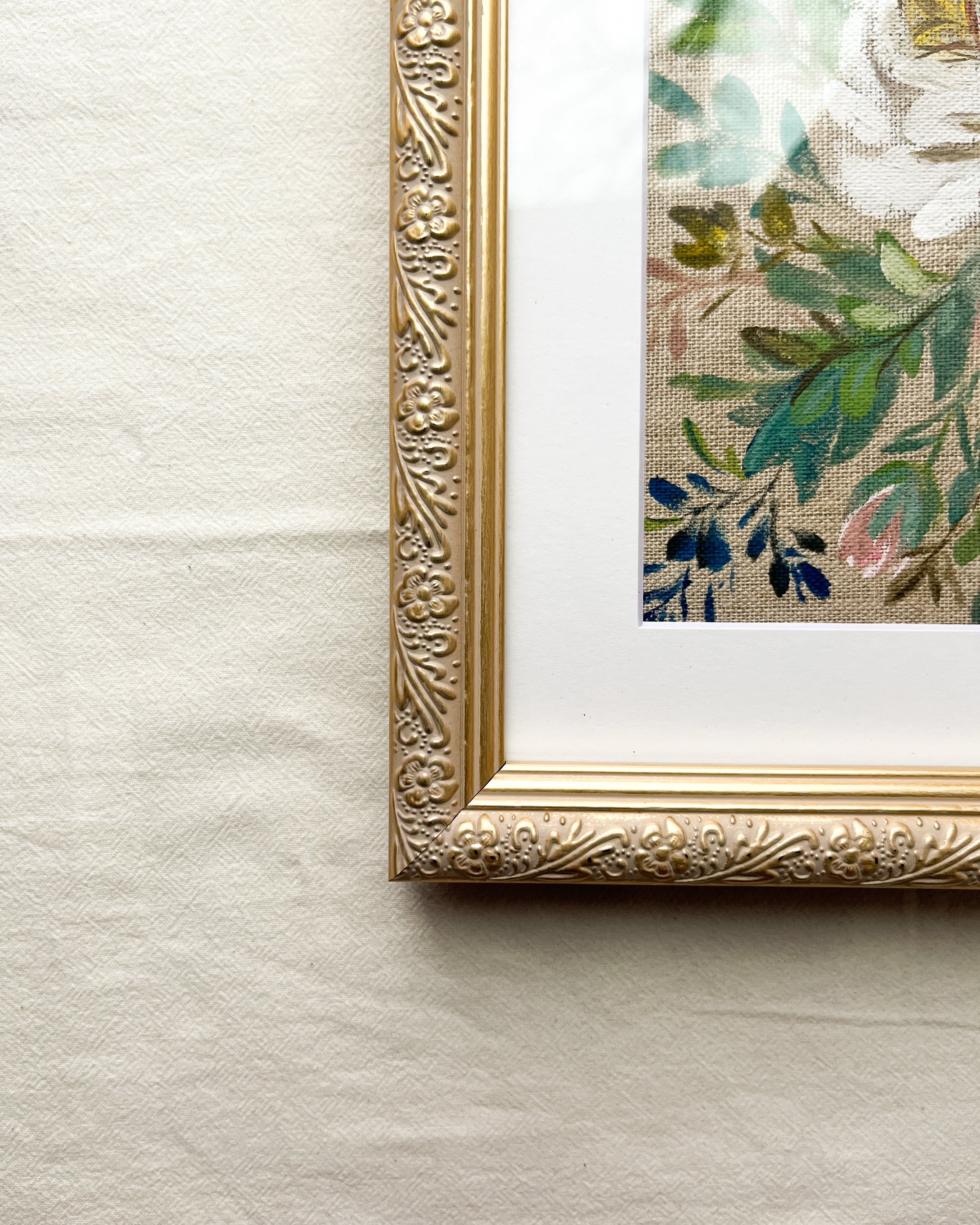 Close-up of subtly distressed champagne gold-tone metal frame with delicate embossed floral detailing on Rooted in Grace rose watercolor painting by Trisha Patel, botanical art.