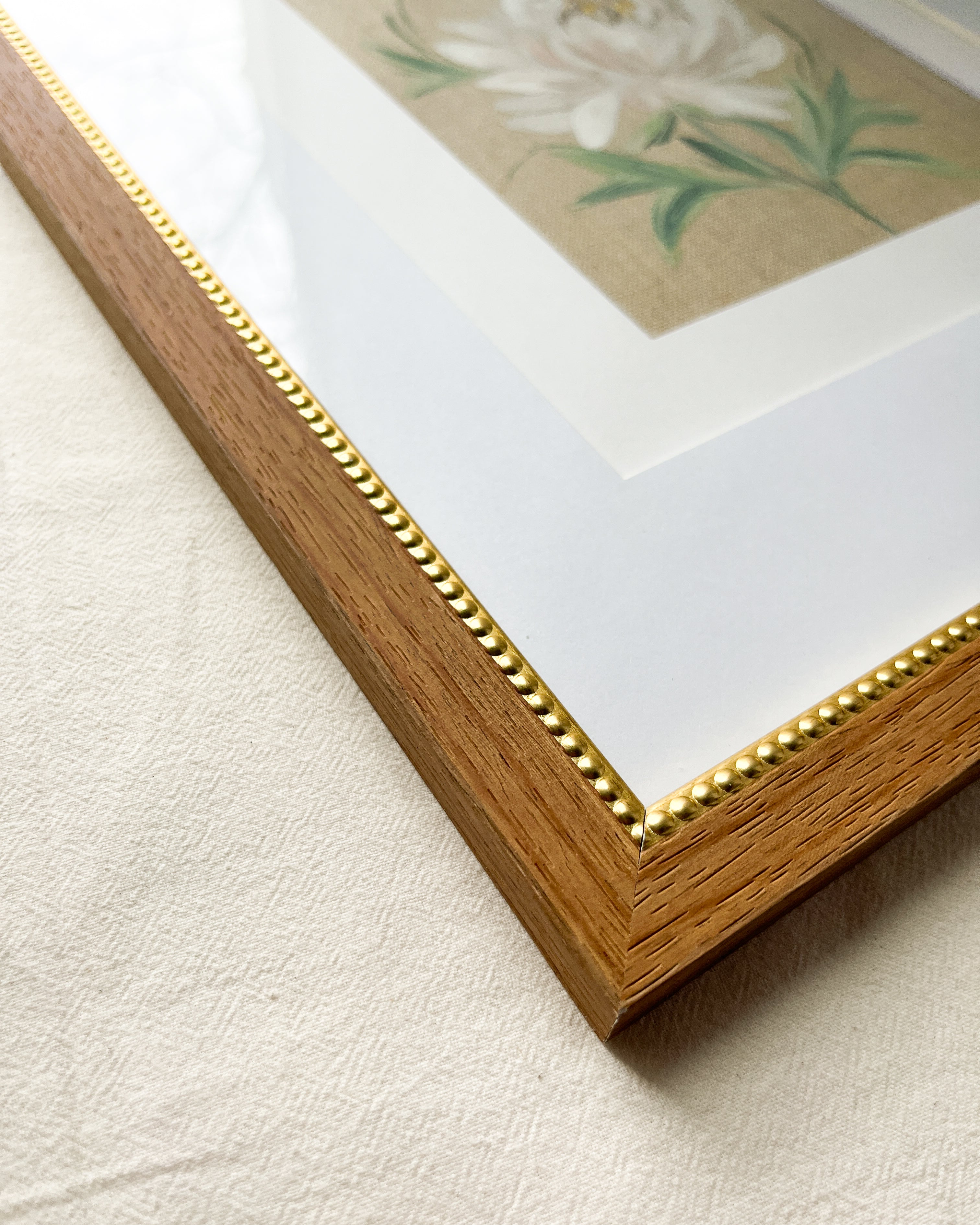 Close-up of warm-toned natural wood frame with gold beaded inner trim on Unfolding Grace peony watercolor painting by Trisha Patel, botanical wall art