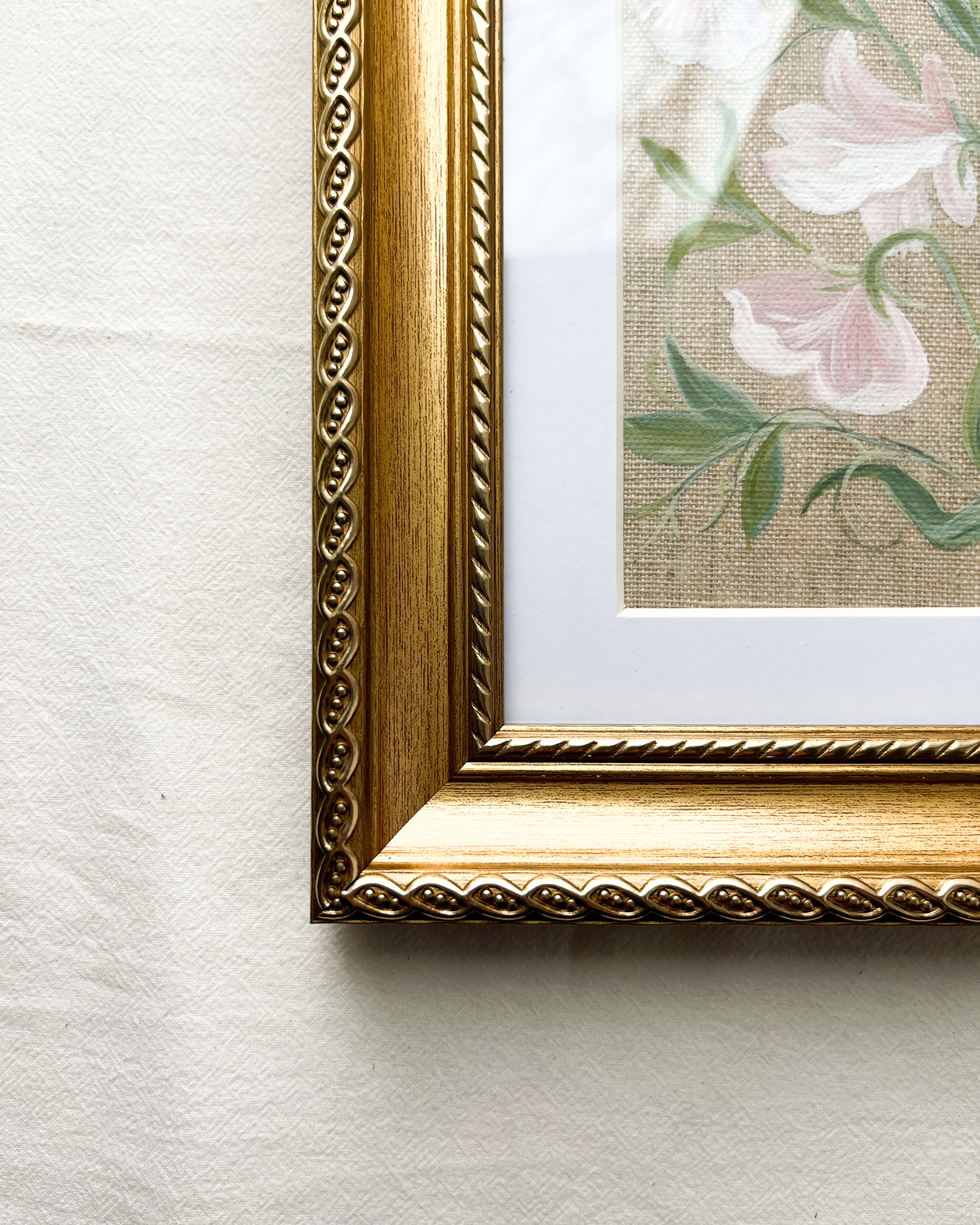 Close-up of gold-toned wooden frame with timeless rectangular shape and elegant rope-inspired border on sweet pea watercolor painting by Trisha Patel, botanical art.