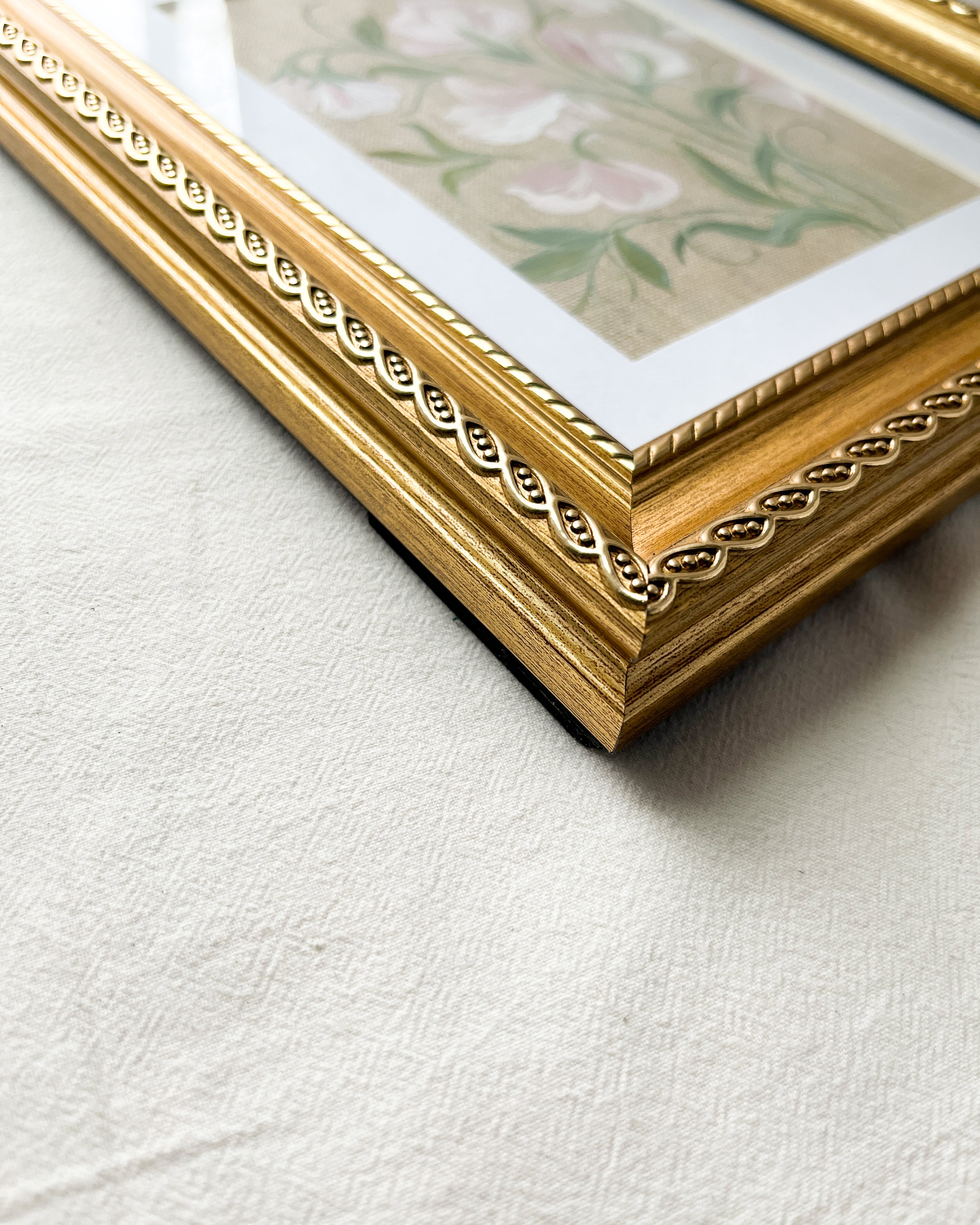 Detailed close-up of vintage-style gold-toned wooden frame featuring rope-inspired edging around sweet pea watercolor artwork by Trisha Patel.