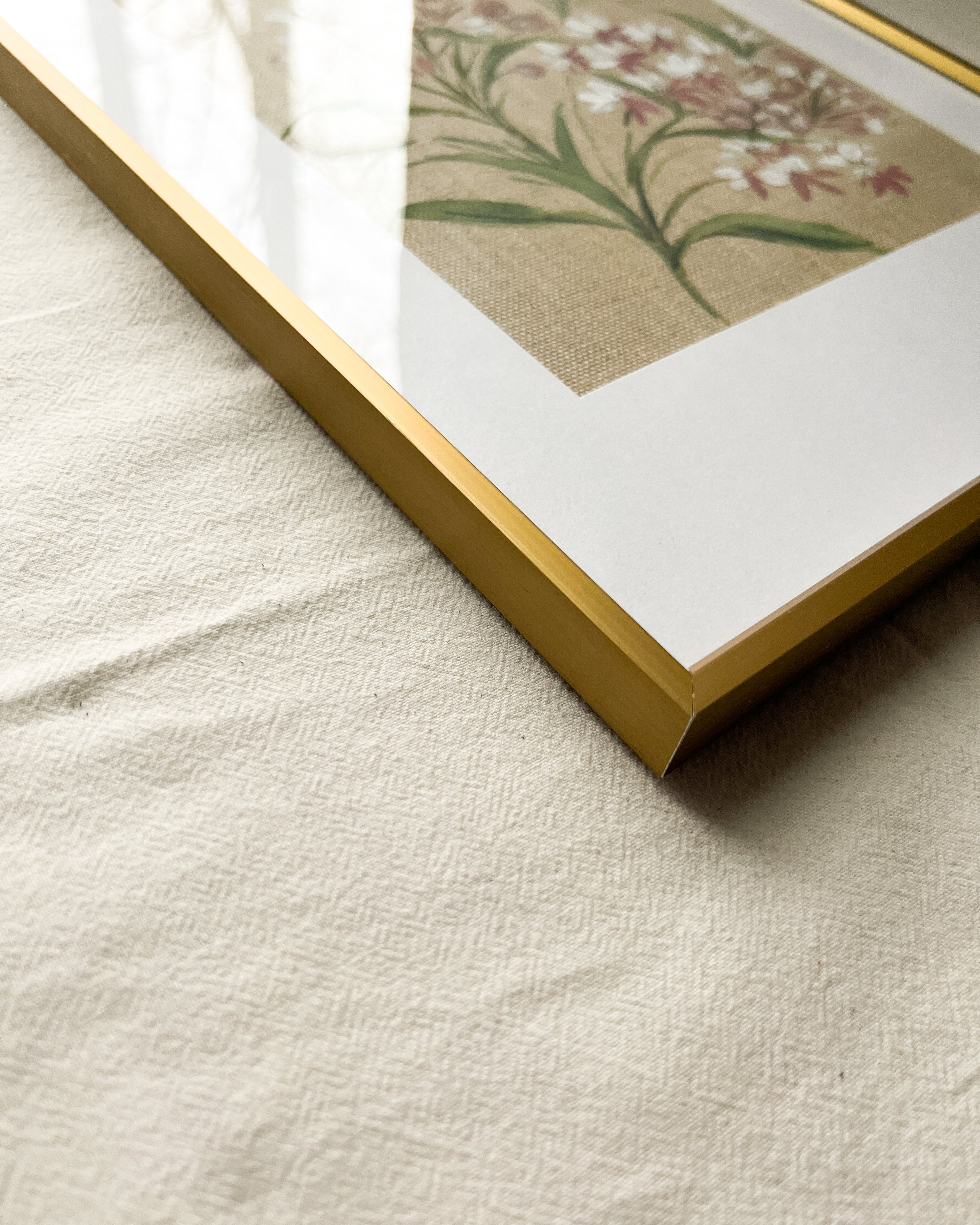 Close-up of sleek gold metal frame with smooth finish and glass on Wings of Change Asclepias watercolor painting by artist Trisha Patel, elegant botanical art display.